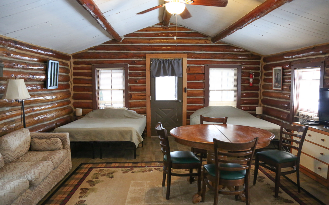 Alternate view of small cabin main room with two queen beds, fold out couch, table and chairs.