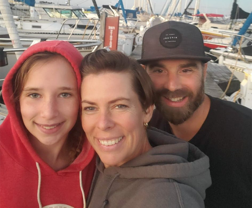 Family picture of a daughter, mother and father with boats in the background.