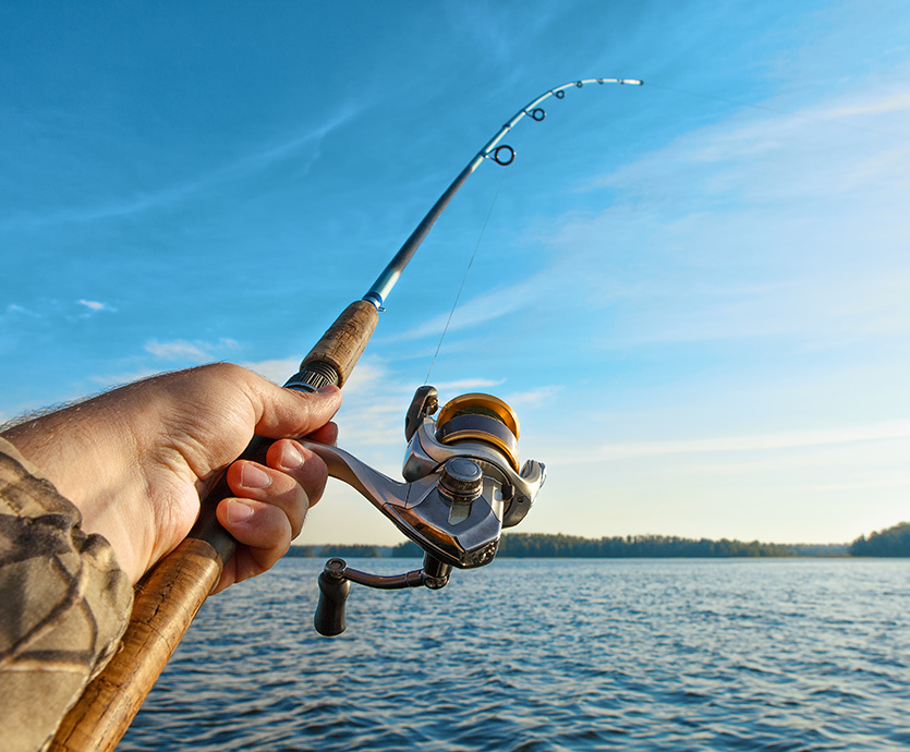 Hand holding out a fishing rod over water.